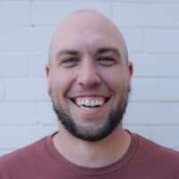 Smiling man in front of brick wall.